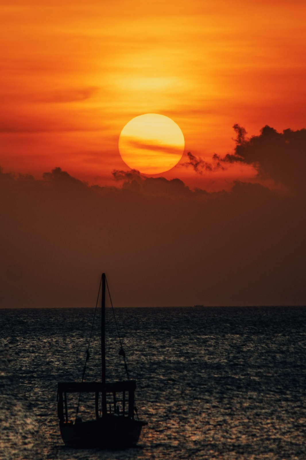 Traditional Zanzibar dhow sailing boat silhouetted against a vivid orange sunset over the Indian Ocean